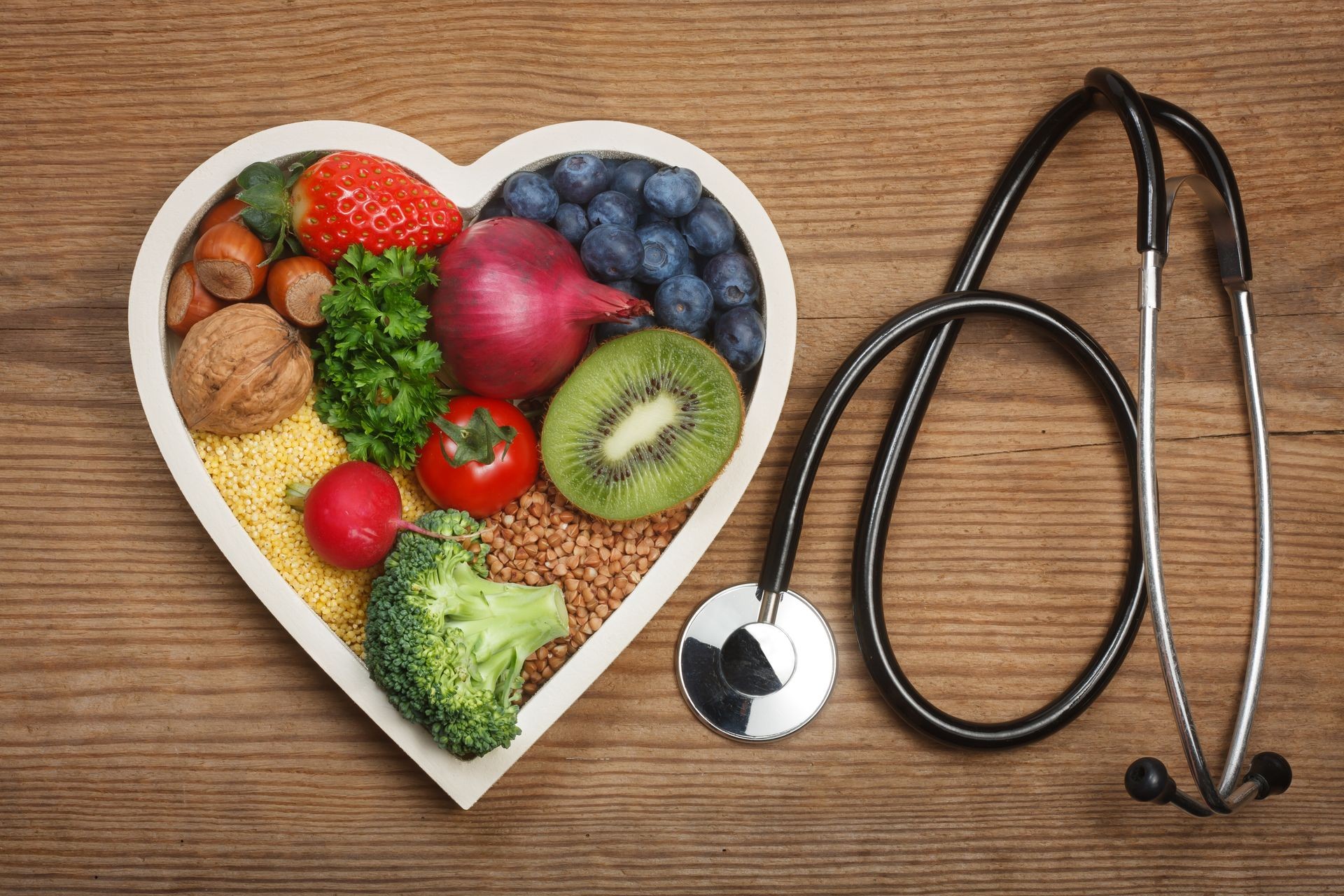 Healthy food in heart shaped bowl and stethoscope. Food such as blueberries, red onion, strawberry, parsley leaves, hazelnuts, walnut, tomato. kiwi, millet, buckwheat, radish, broccoli. Healthy food in heart shaped bowl and stethoscope. Food such as blueberries, red onion, strawberry, parsley leaves, hazelnuts, walnut, tomato. kiwi, millet, buckwheat, radish, broccoli.